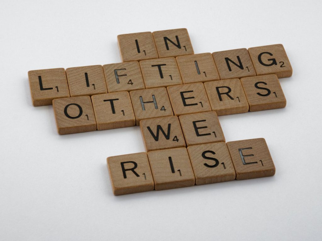 scrabble tiles spelling out "in lifting others we rise"